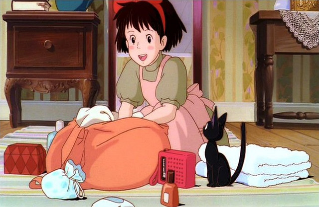 Kiki packs excitedly for her journey while her familiar, the black cat Jiji, looks on.